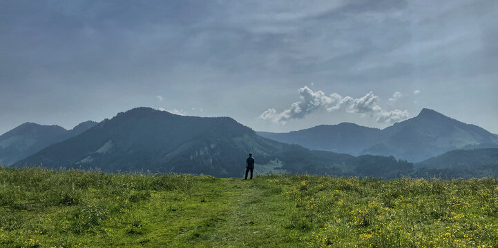 Wanderer steht am Horizont und blickt auf eine Alpensilhouette