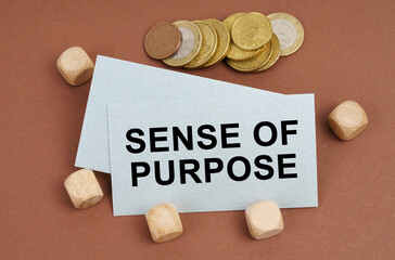 On a brown surface are coins, cubes and a business card with the inscription - Sense of Purpose