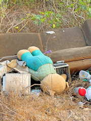 Large brown sofa, soft teddy bear are thrown out in trash heap in summer outdoors. Pollution of nature, environment, garbage. Poor ecology in Cyprus, Paphos city. Stuffed animals are thrown away