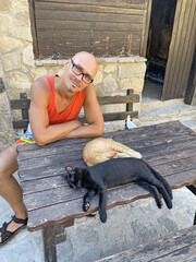 Young handsome man sits next to cats. Two young kittens of black and red color are sleeping sweetly on a wooden table in Cyprus. Street cats sleep in nature. Brother and sister