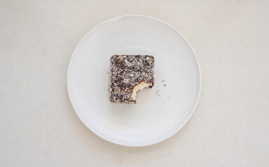 High angle view of partly eaten lamington cake on white plate with crumbs (selective focus)