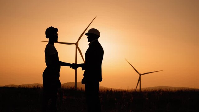 Silhouette man shaking hands with engineer with wind turbines on background. Heartwarming uplifting picture of clean energy for the environment. Two colleagues making deal about successful cooperation