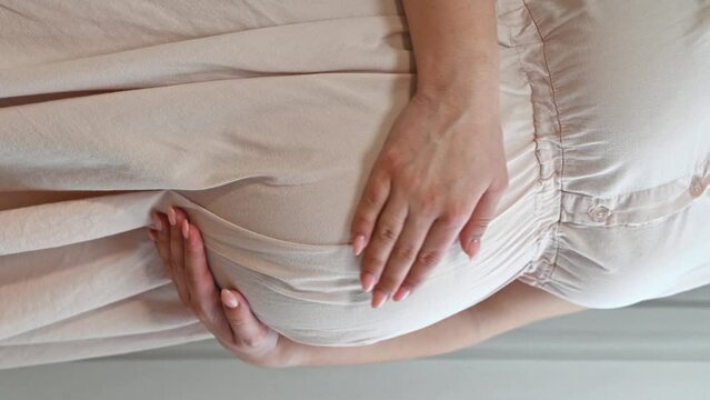 Vertical footage of young pregnant woman holding the belly. Expecting a child, motherhood concept	
