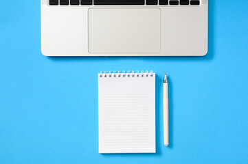 Fototapeta na wymiar Silvery laptop and notepad with a blank white sheet on a blue background. Flat lay, copy space.