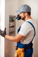 Electrical technician in uniform looking focused while checking fuses in a switchboard