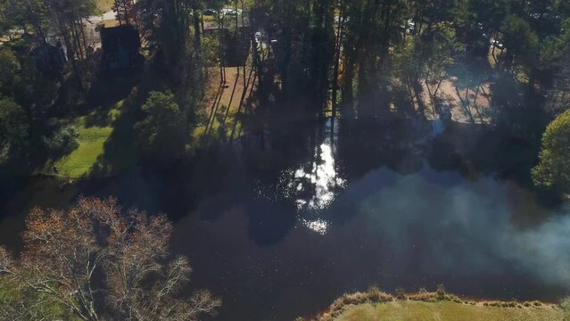 Aerial drone fly over of small lake with a glimpse of sun.