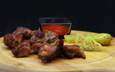 Pieces of fried pork with onions and herbs, green pepper slices and tomato sauce on a serving board. Against a dark background with shallow depth of field