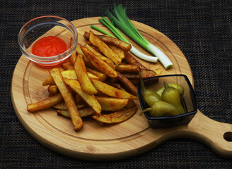 French fries on a serving board rimmed with containers of ketchup, green peppers and green onions