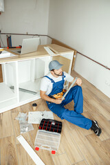 Hign angle view of handyman in overalls holding a part of cabinet while installing kitchen...