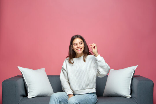 Smiling young girl shows little size gesture with fingers, sitting on couch. Small prices, shopping sales discounts