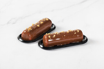 Moderne Chocolate walnut cake in the form of a cylindrical bar, with mirror glaze on a serving plate on a white background