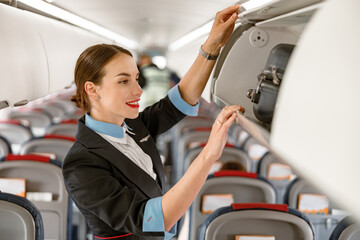 Joyful stewardess checking overhead luggage bin in airplane