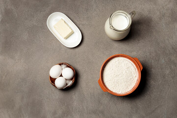 Ingredients for making the dough. Milk, butter, eggs and flour. Top view on a gray background.