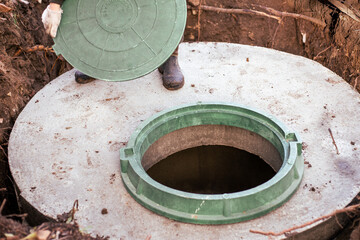 The plumber covers the sewer well with a manhole cover. Water supply and sewerage in a residential...