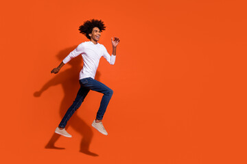 Fototapeta na wymiar Photo of charming sweet guy wear white shirt jumping high running fast empty space isolated orange color background