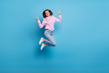 Fototapeta premium Photo of pretty excited woman wear striped sweater jumping up v-sings empty space isolated blue color background