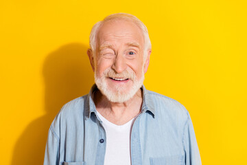 Portrait of attractive cheerful grey-haired man good mood winking isolated over bright yellow color...