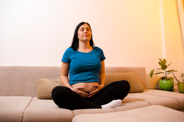 Young pregnant woman practicing breathing techniques , yoga or meditation in her living room 
