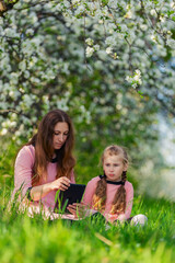 mother with daughter and tablet in blooming apple orchard