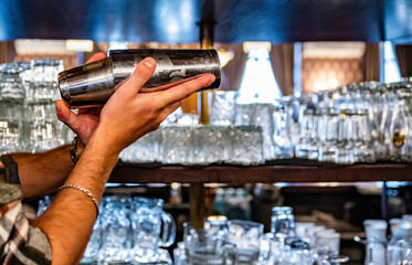 man bartender at bar holds steel shaker in her hands, shakes it to make cocktail.