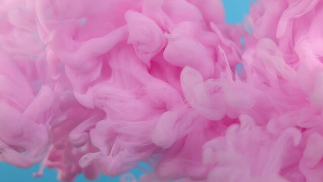 A pink cloud of colors slowly moving in the water on a blue background.