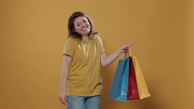 Portrait of woman feeling proud of purchase showing excitement for buying products in studio. Smiling person holding shopping bags feeling ecstatic and pleased with aquisition over yellow background.