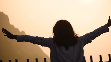 Silhouette of Indian young woman raising hand against Girnar hill during time of sunrise. Woman successfully  hiking on mountain and enjoying view. Concept of travel and adventure  