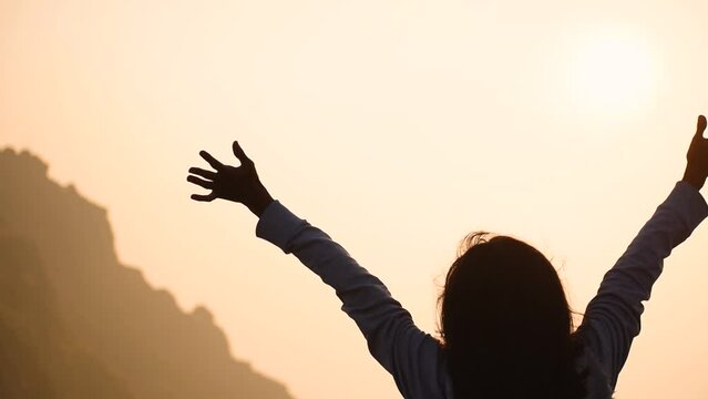 Silhouette of Indian woman celebrating success while standing against Girnar hill with sun in sky during time of sunrise. Woman successfully hiking mountain and enjoying view. Travel and adventure  
