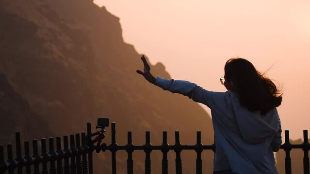 Silhouette of Indian young woman raising hand against Girnar hill during time of sunrise. Woman successfully  hiking on mountain and enjoying view. Concept of travel and adventure  