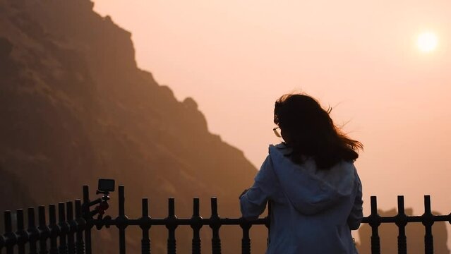 Silhouette of Indian young woman raising hand against Girnar hill during time of sunrise. Woman successfully  hiking on mountain and enjoying view. Concept of travel and adventure  