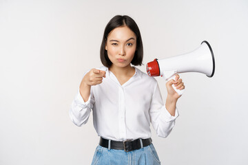 Image of modern asian woman with megaphone, pointing at you camera, making announcement, white...