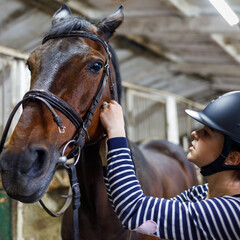 Teenage girl horse rider adjusting reins in harness at the stable.