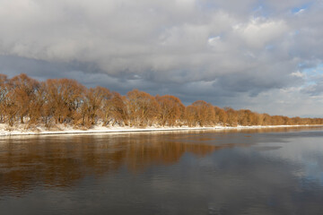 View of the river on a sunny winter day. Trees on the banks of the river illuminated by bright sunlight.