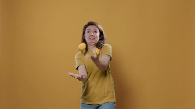 Playful woman acting silly trying to juggle oranges being funny while dropping them in studio. Individuality concept of person with fun and goofy personality showing juggle talent.