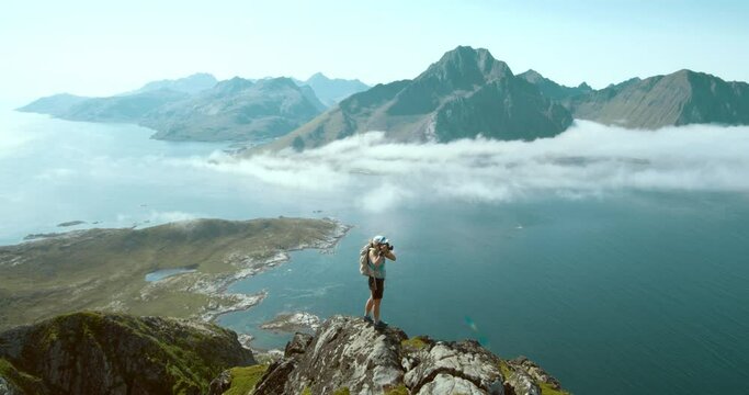 Epic landscape panorama and young female hiker on top of mountain summit over lofoten fjords. Woman photographer during travel road trip to norway outdoor destinations. Wanderlust lifestyle