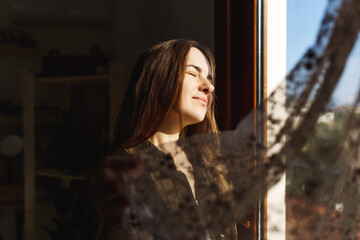 Pretty young woman in apartment opening window curtains after wake up, enjoying morning sunshine .Mental health concept .