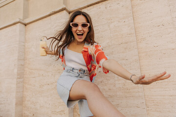 Cheerful caucasian dark-haired girl fooling around lot in the fresh air against background of wall....