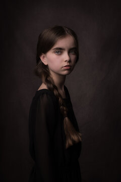 Classic dark studio portrait of young girl in black dress in old masters style