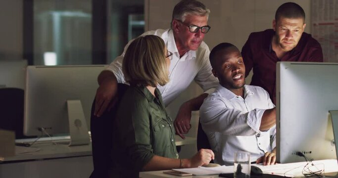 Business group of diverse colleagues using computer and discussing work at a table during a late night in a modern office