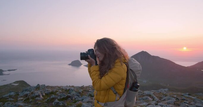 Portrait of female travel photographer shoot sunset on mountain top summit. Norwegian midsummer midnight sun. adventure wanderlust lifestyle. Young woman on outdoor hiking trip.Content creator blogger