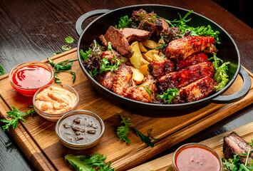 Different barbecue meat with potatoes in a frying pan