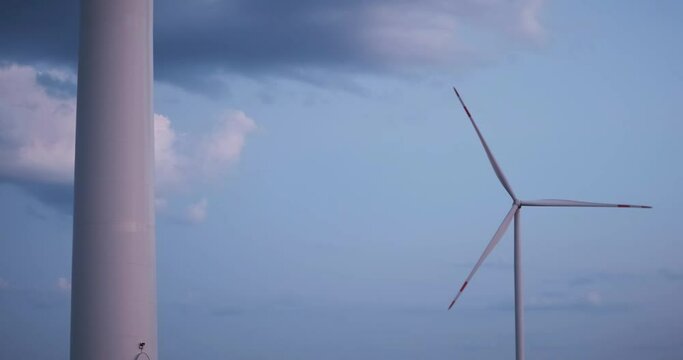 Cinematic calm windmill scene with beautiful sunset sky. Green energy wind generator slowly rotating blades. Industrial eco power supply station in a landscape field. Ecology friendly new technology.