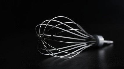 Steel whisk of a hand blender on a black background. Macro. The concept of attachments for a...