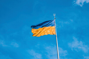 Ukrainian bicolor yellow blue national flag with trident emblem waving in wind against sky,...