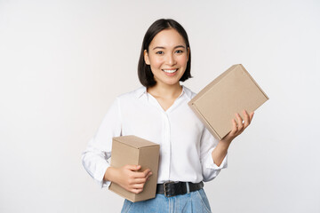 Concept of shopping and delivery. Young happy asian woman posing with boxes and smiling, standing over white background - obrazy, fototapety, plakaty