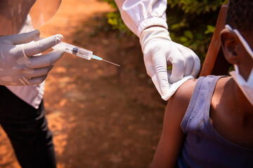 Close-up of a doctor's hand with a syringe about to inject the vaccine to a child in africa....