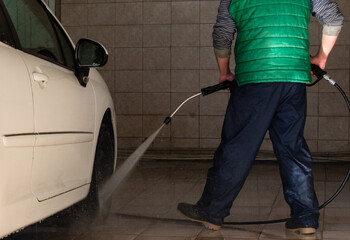 Fototapeta premium Guy washing white car with powerful water jet in open garage box