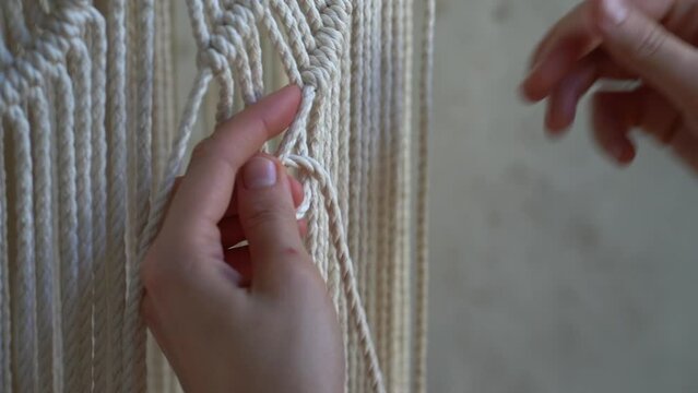 Closeup hands of freelancer woman working on half-finished macrame piece, weaves lamp shade for chandelier. Women hobby.
