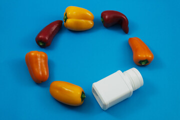 Colorful mini sweet peppers and a white jar with vitamins on a blue background