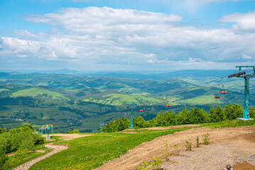 Fototapeta premium Winding dirtroad and ski lifts on grassy covered hill of countryside on summer day, Mountain road beside chair lifts with beautiful rural landscape
